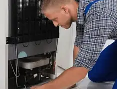 Refrigerator repair technician servicing the compressor and condenser area in Jackson, MS